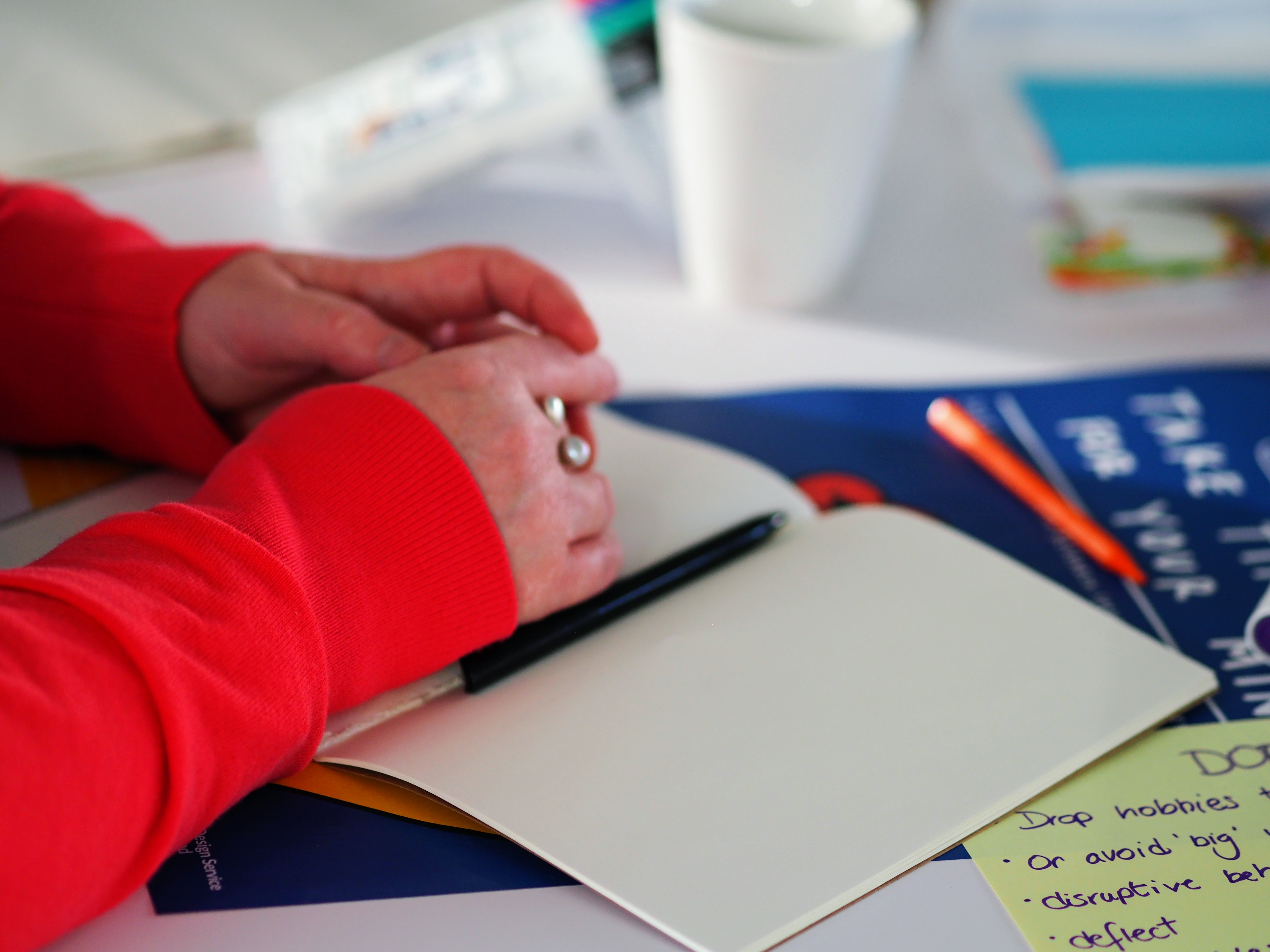 Hands at rest next to a pen and notebook.